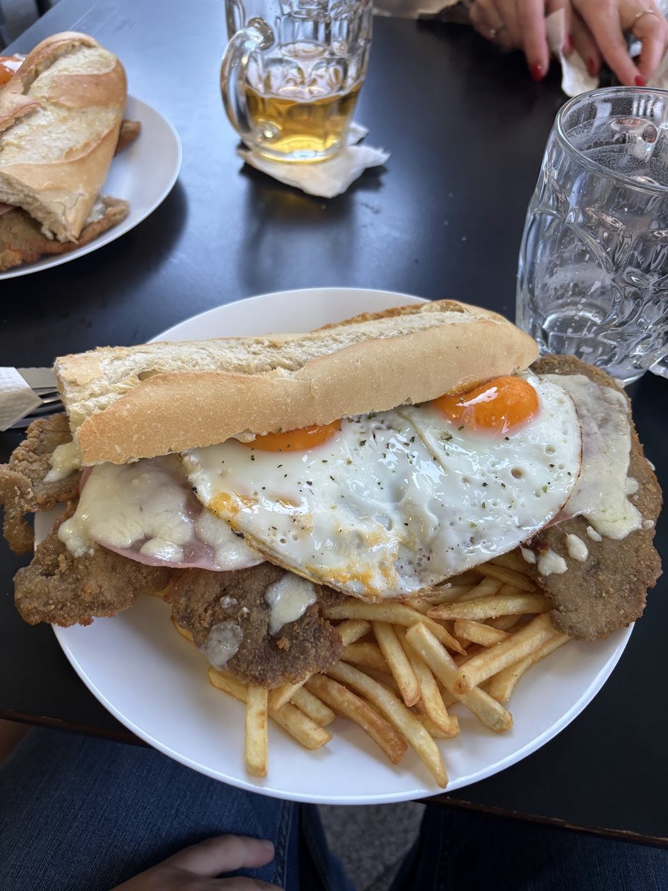 Bocadillo de milanesa con huevo frito y patatas, servido en pan de barra.